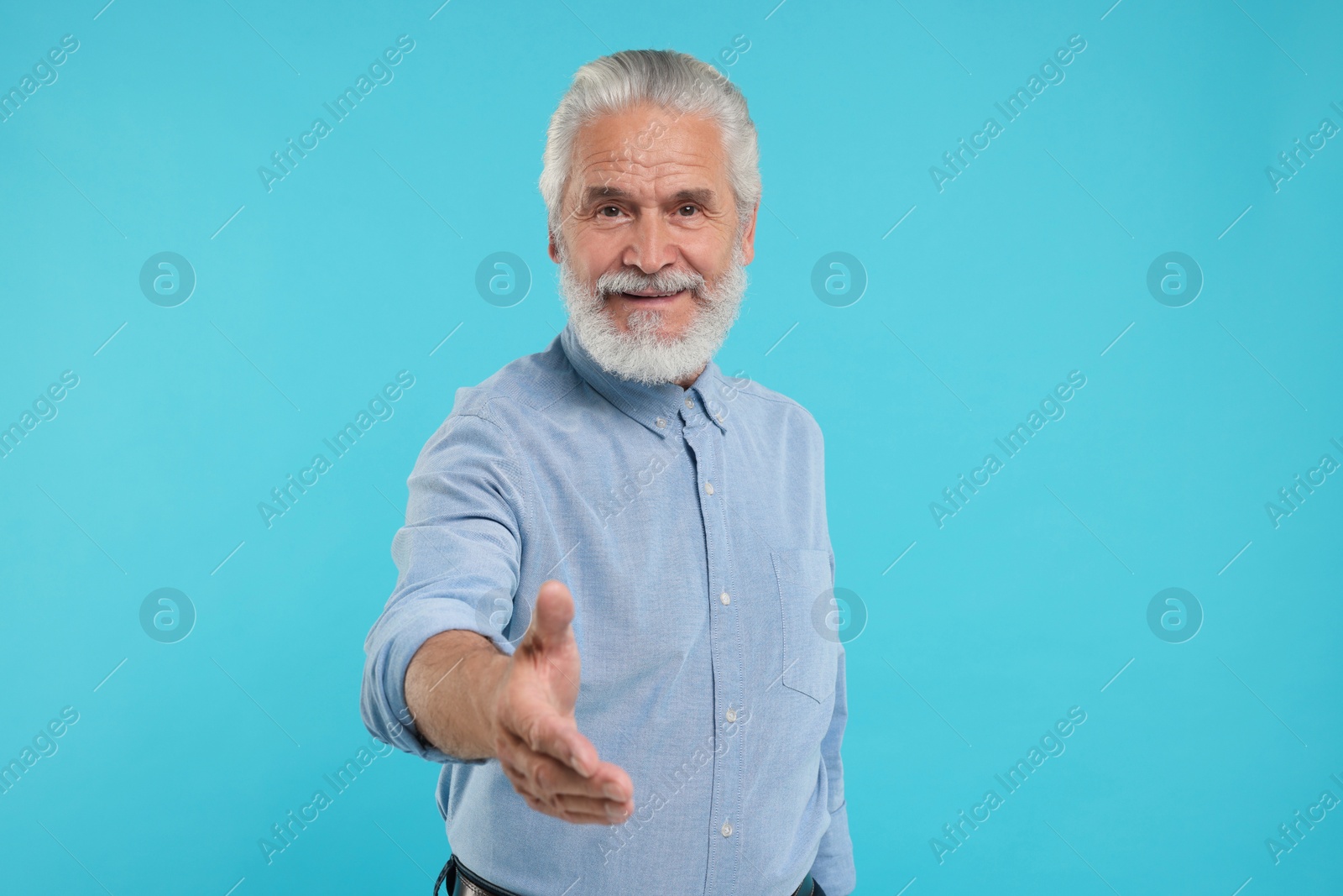 Photo of Senior man welcoming and offering handshake on light blue background