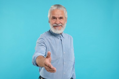 Photo of Senior man welcoming and offering handshake on light blue background