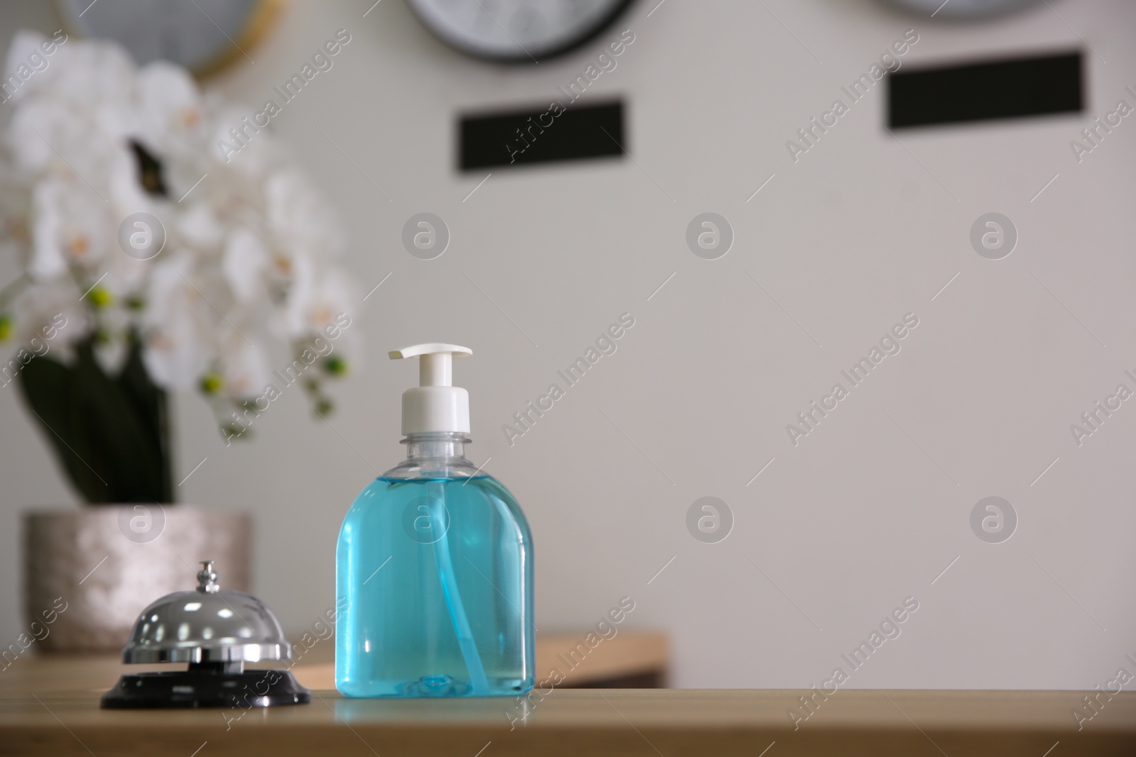 Photo of Dispenser bottle of antiseptic gel and service bell on reception desk in hotel. Space for text