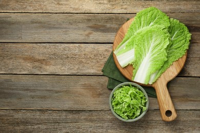 Photo of Cut fresh Chinese cabbage and leaves on wooden table, top view. Space for text