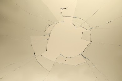 Photo of Closeup view of broken glass with cracks on beige background