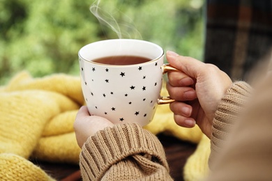 Image of Woman with cup of hot tea near window sill indoors, closeup
