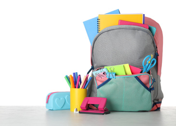 Bright backpack with school stationery on grey stone table against white background