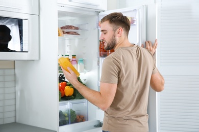 Photo of Man taking bottle with juice out of refrigerator in kitchen