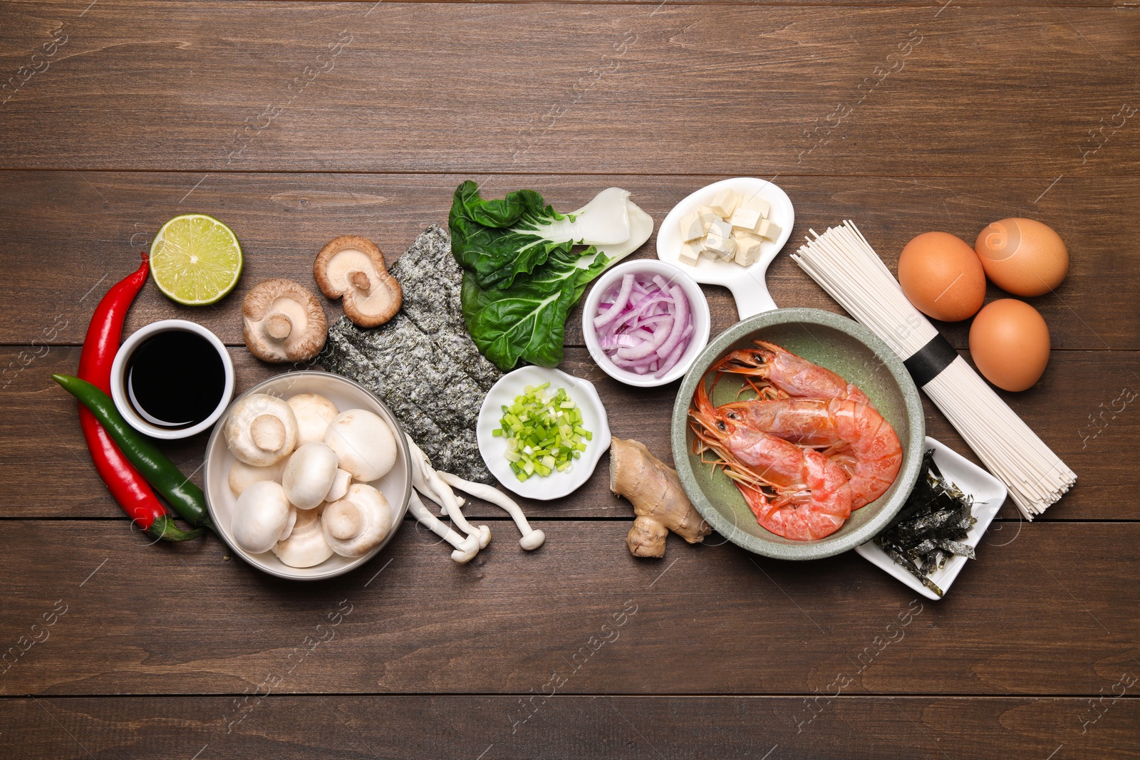 Photo of Cooking delicious ramen soup. Different ingredients on wooden table, flat lay