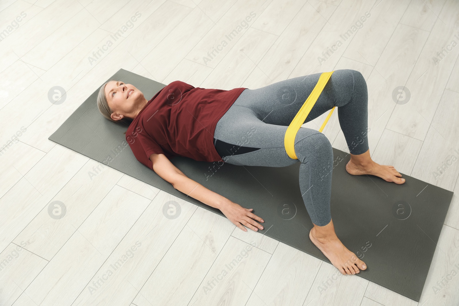 Photo of Senior woman doing exercise with fitness elastic band on mat at home