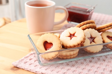 Photo of Traditional Christmas Linzer cookies with sweet jam and cup of tea on table