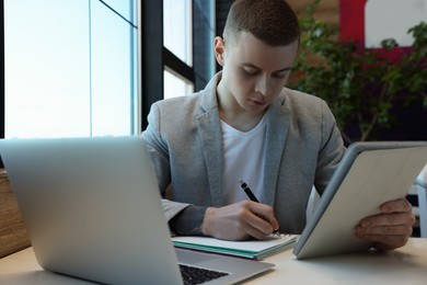 Photo of Young male student with laptop and tablet studying at table in cafe