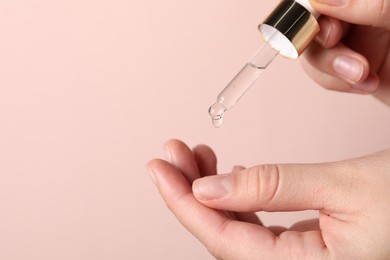 Photo of Woman applying cosmetic serum onto fingers on light pink background, closeup. Space for text