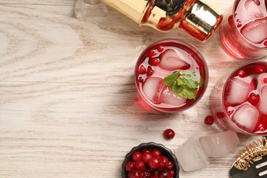 Photo of Tasty cranberry cocktail with ice cubes in glasses and bartender's tools on wooden table, flat lay. Space for text
