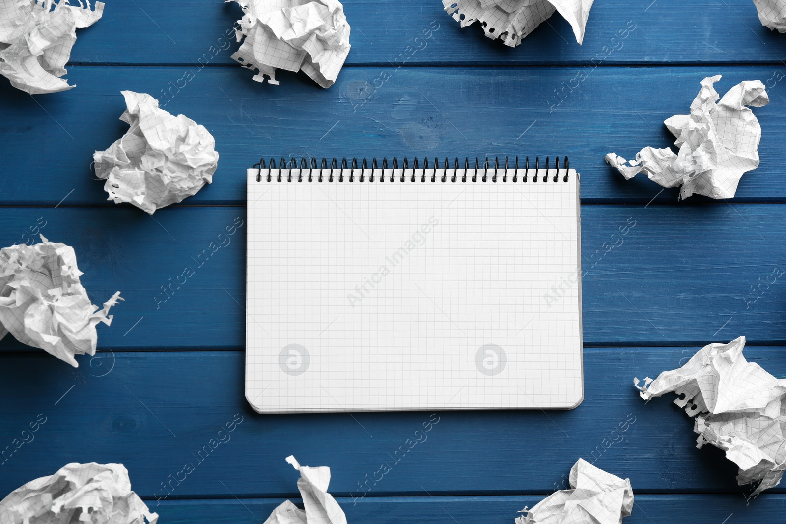 Photo of Notebook and crumpled sheets of paper on blue wooden background, flat lay. Space for text