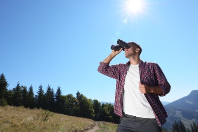 Man looking through binoculars in mountains on sunny day, low angle view