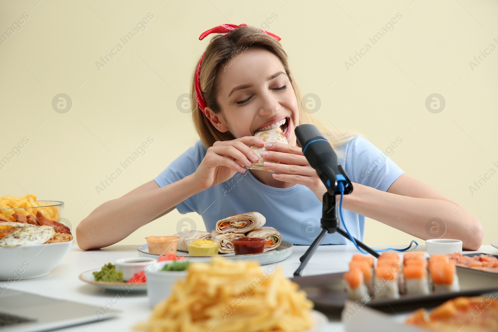 Photo of Food blogger eating in front of microphone at table against light background. Mukbang vlog