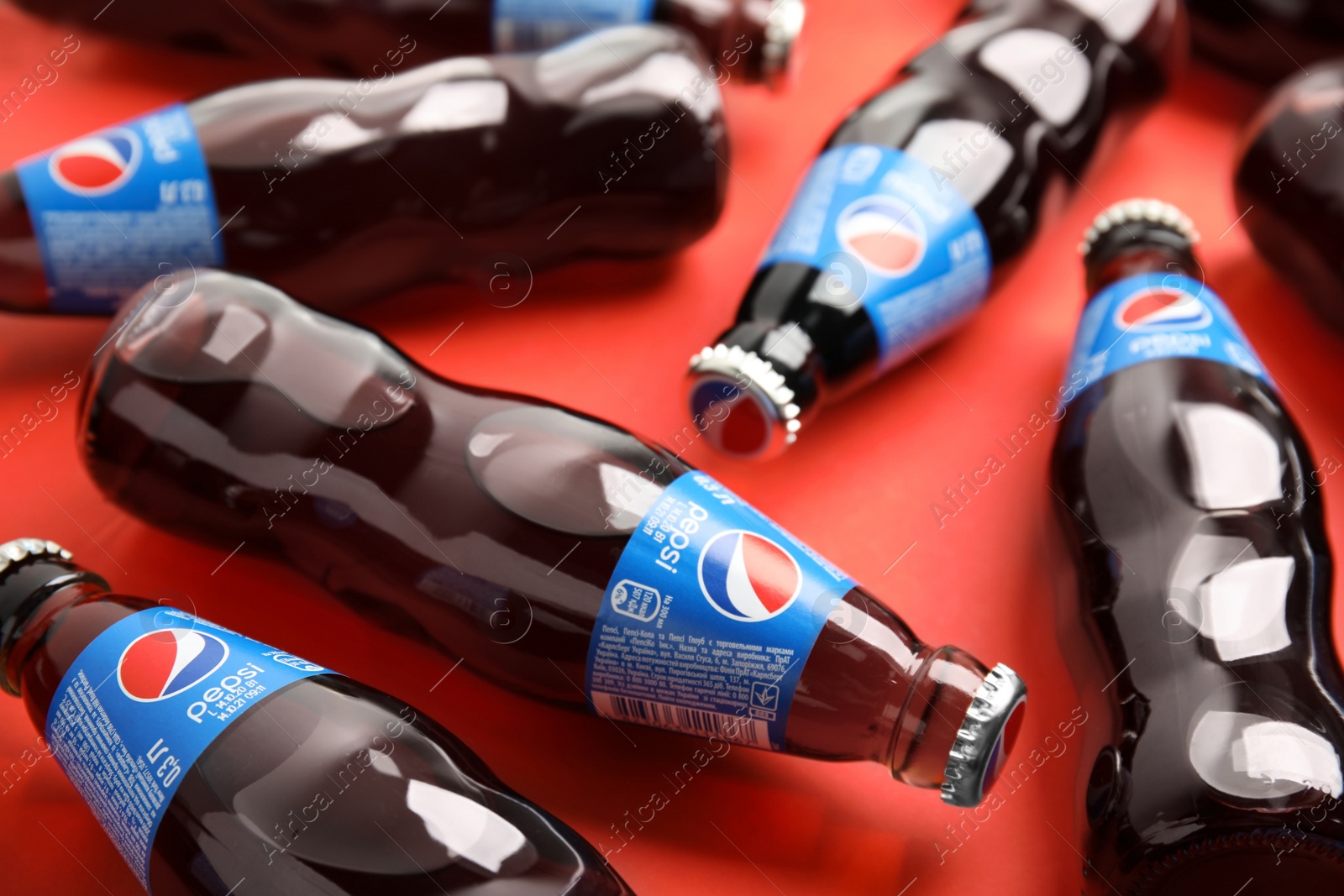 Photo of MYKOLAIV, UKRAINE - FEBRUARY 08, 2021: Glass bottles of Pepsi on red background, closeup