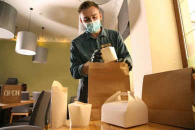 Photo of Waiter packing takeout order in restaurant. Food service during coronavirus quarantine