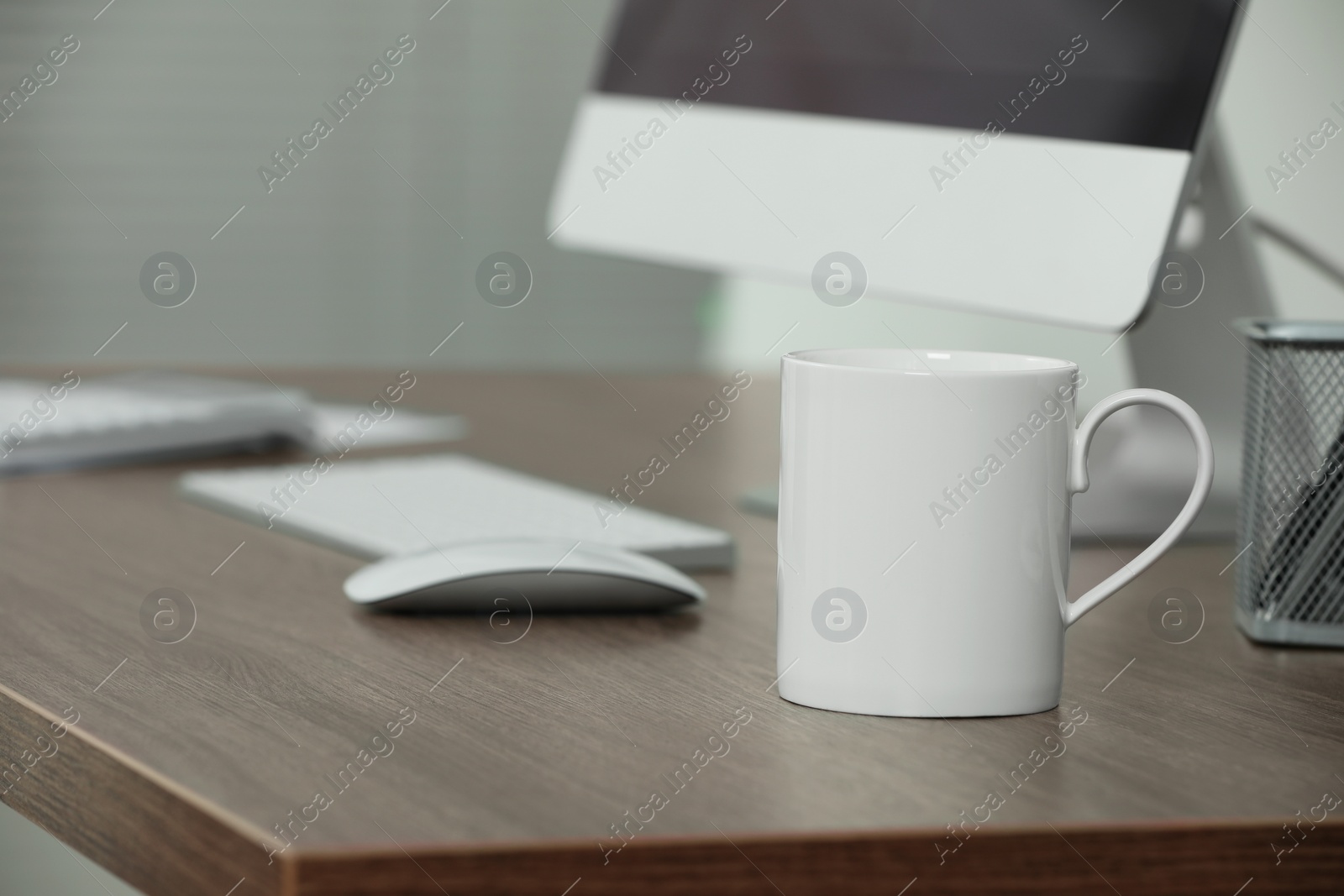 Photo of White ceramic mug on wooden table at workplace. Mockup for design