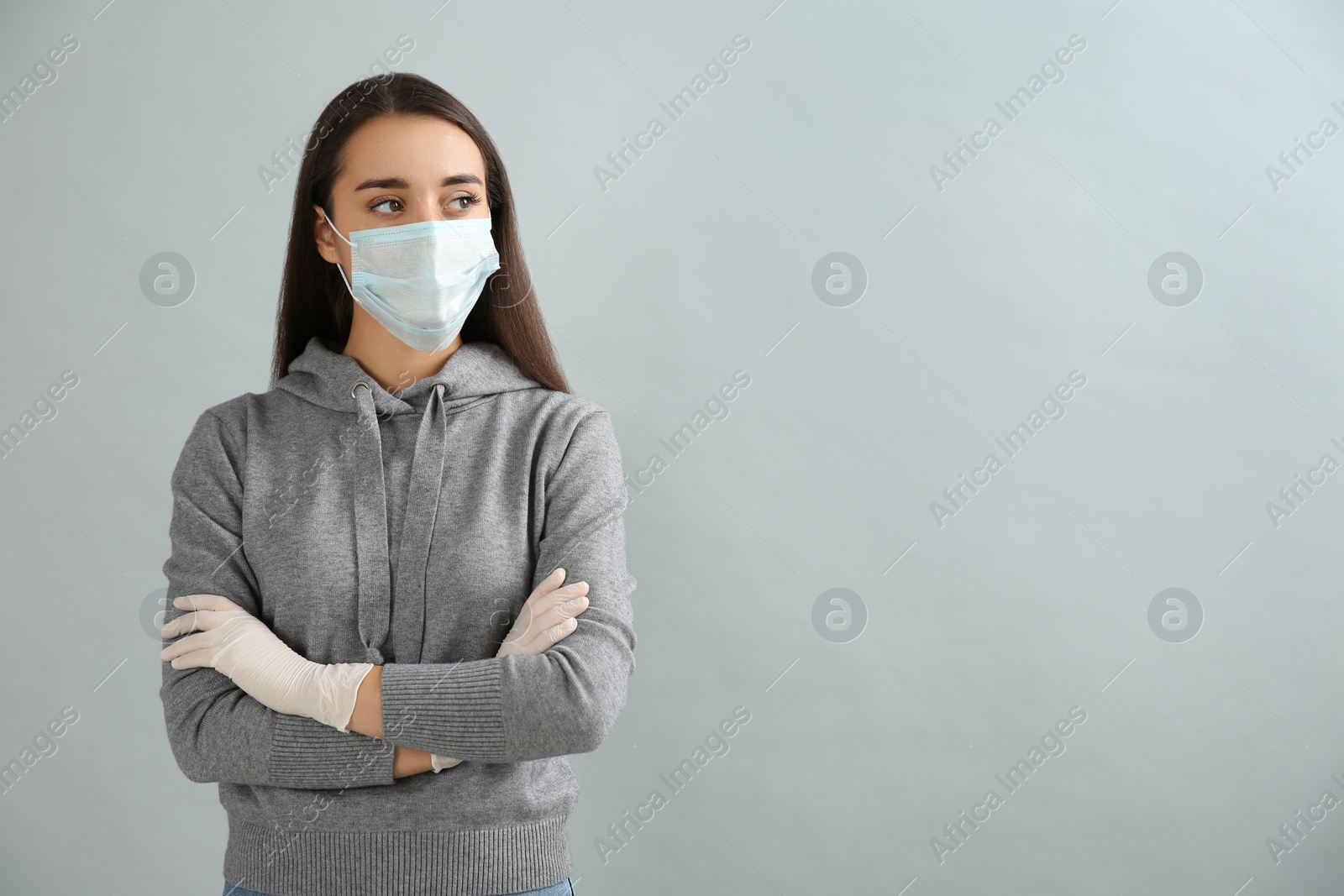 Photo of Woman wearing protective face mask and medical gloves on grey background. Space for text