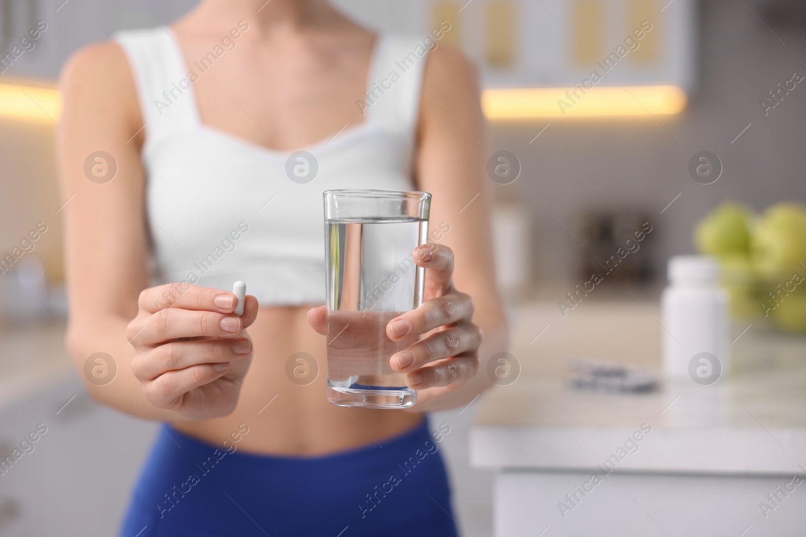 Photo of Woman with pill, glass of water in kitchen, closeup and space for text. Weight loss