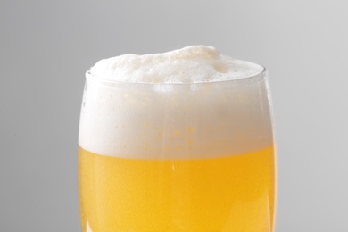 Photo of Glass of tasty beer with foam on color background, closeup