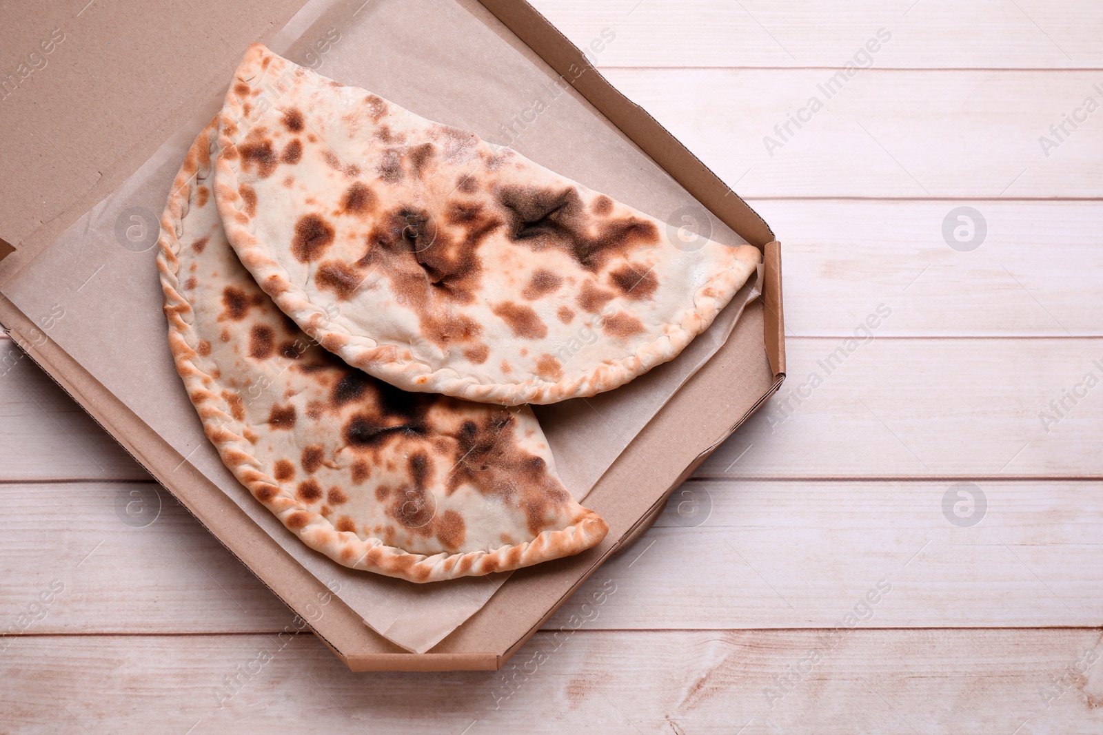 Photo of Cardboard box with delicious calzones on light wooden table, top view. Space for text