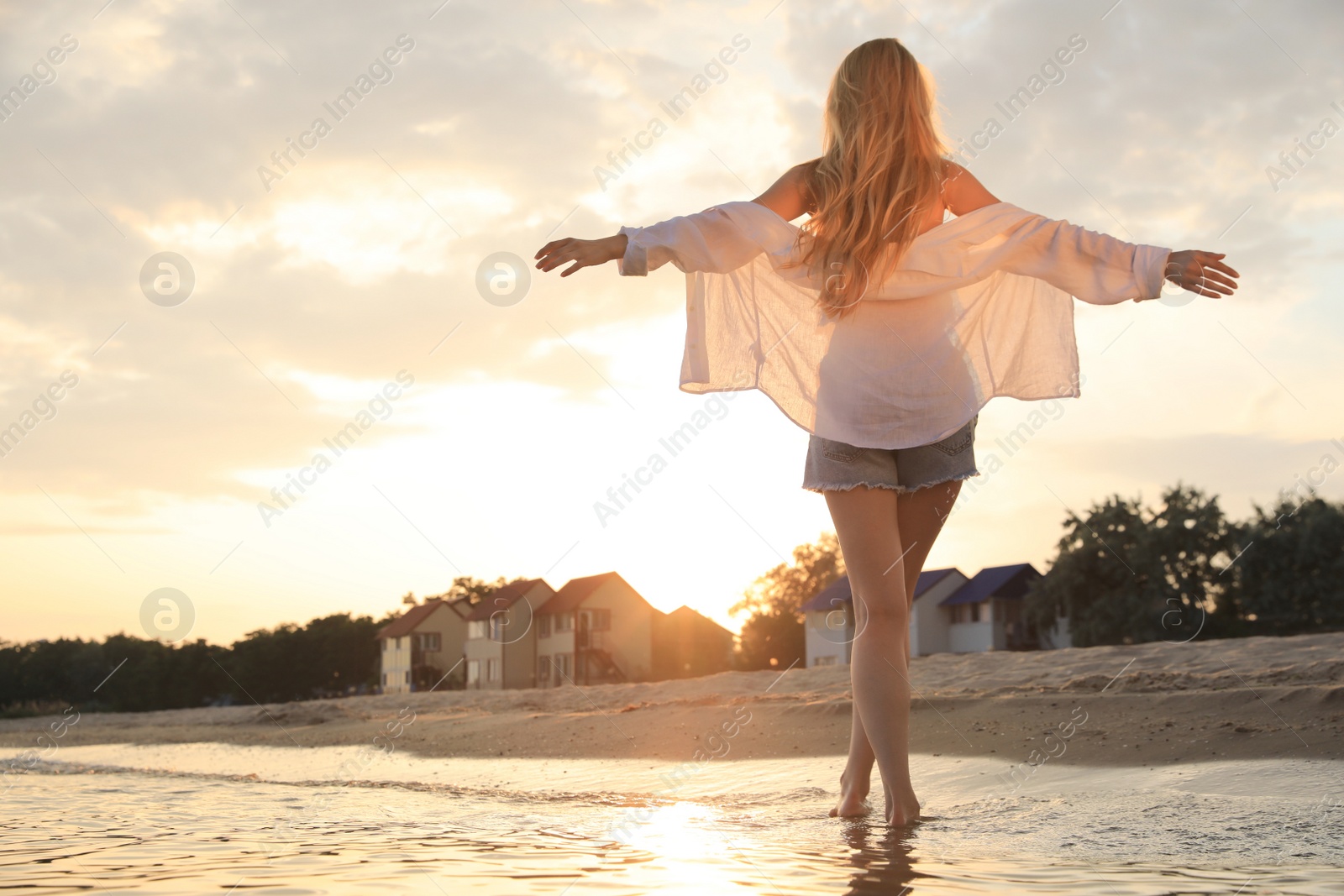 Photo of Beautiful young woman on beach at sunset, back view
