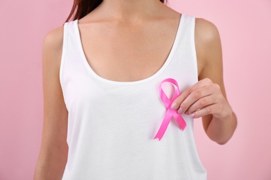 Woman holding pink ribbon on color background, closeup. Breast cancer awareness