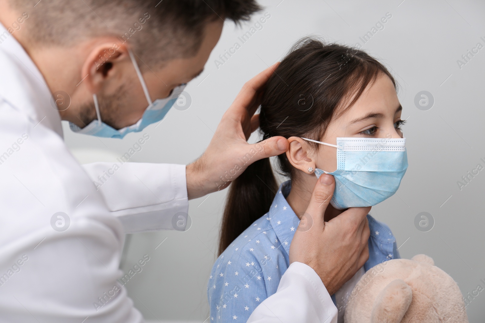 Photo of Pediatrician examining little girl in hospital. Doctor and patient wearing protective masks