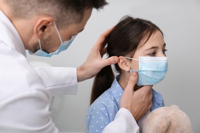 Photo of Pediatrician examining little girl in hospital. Doctor and patient wearing protective masks