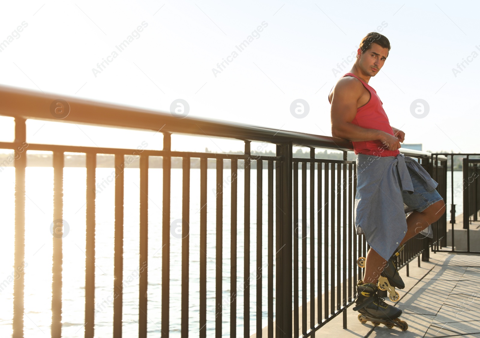 Photo of Handsome young man with roller skates on pier near river, space for text