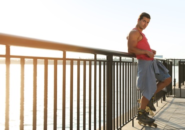 Photo of Handsome young man with roller skates on pier near river, space for text