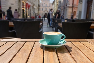 Cup of aromatic hot coffee on wooden table in outdoor cafe, space for text