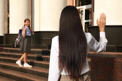 Mother waving goodbye to her daughter near school entrance