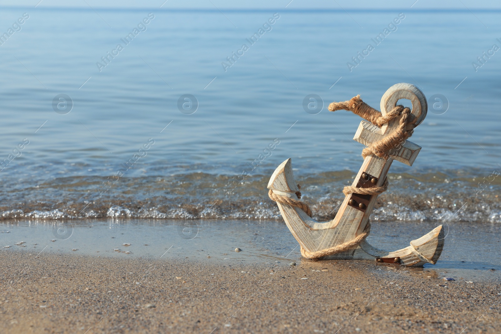 Photo of Wooden anchor with rope on sand near sea. Space for text