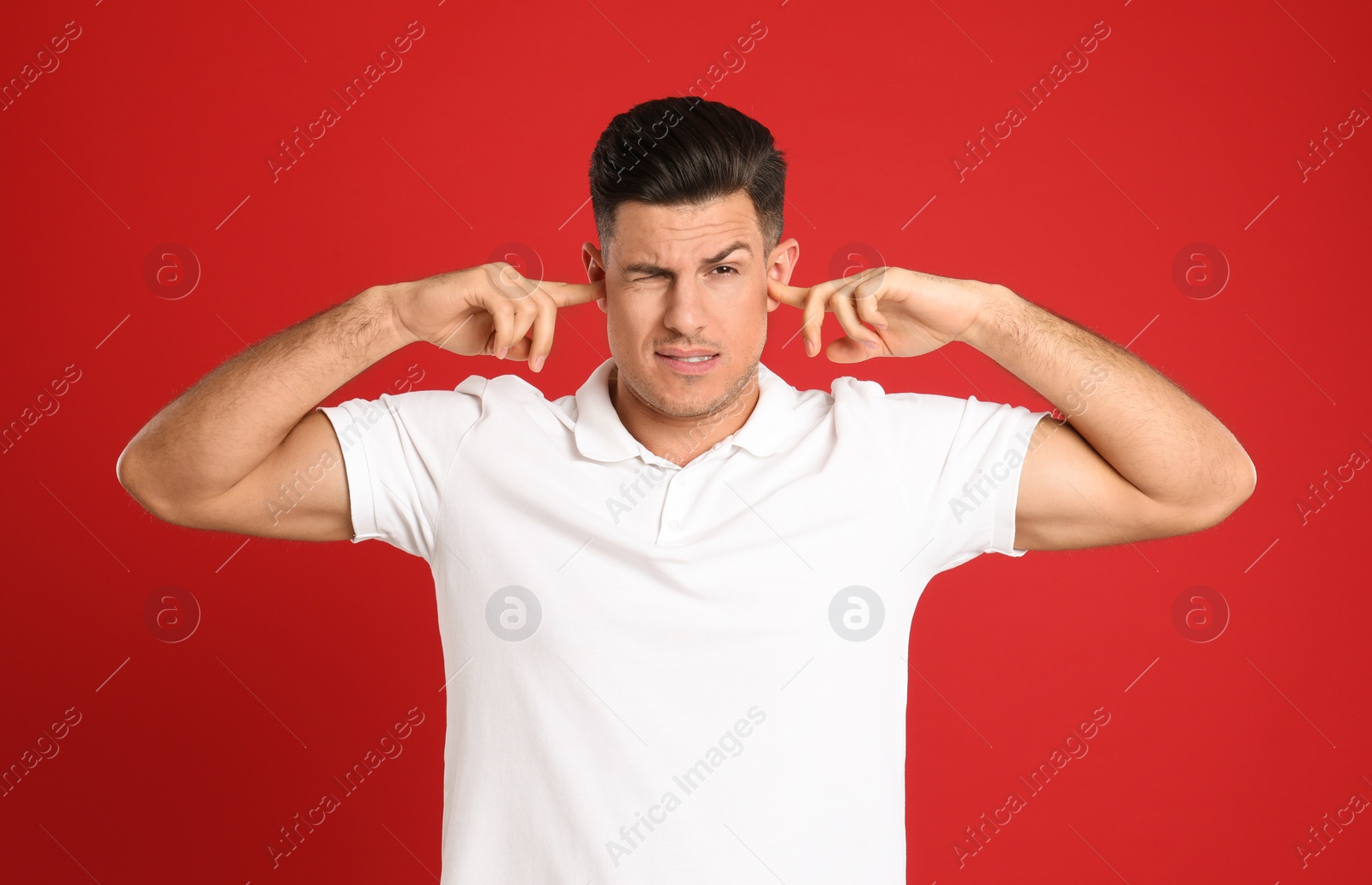 Photo of Man covering ears with fingers on red background