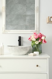 Vase with beautiful pink tulips and toiletries near sink in bathroom