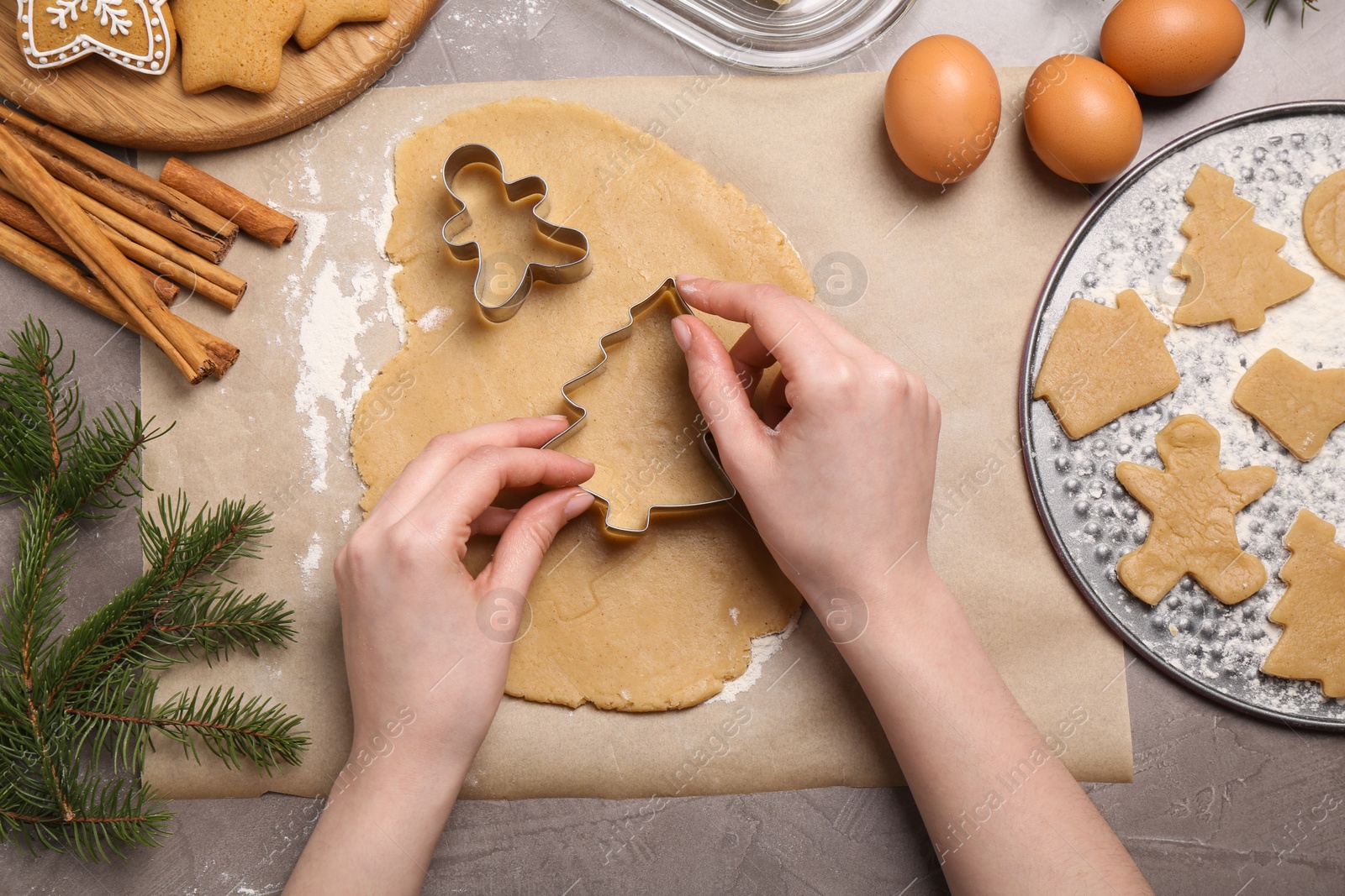 Photo of Woman making Christmas cookies with cutters at grey table, top view