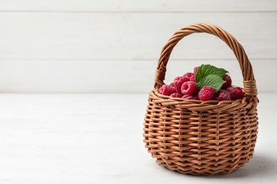 Photo of Basket of delicious fresh ripe raspberries with leaves on white wooden table, space for text