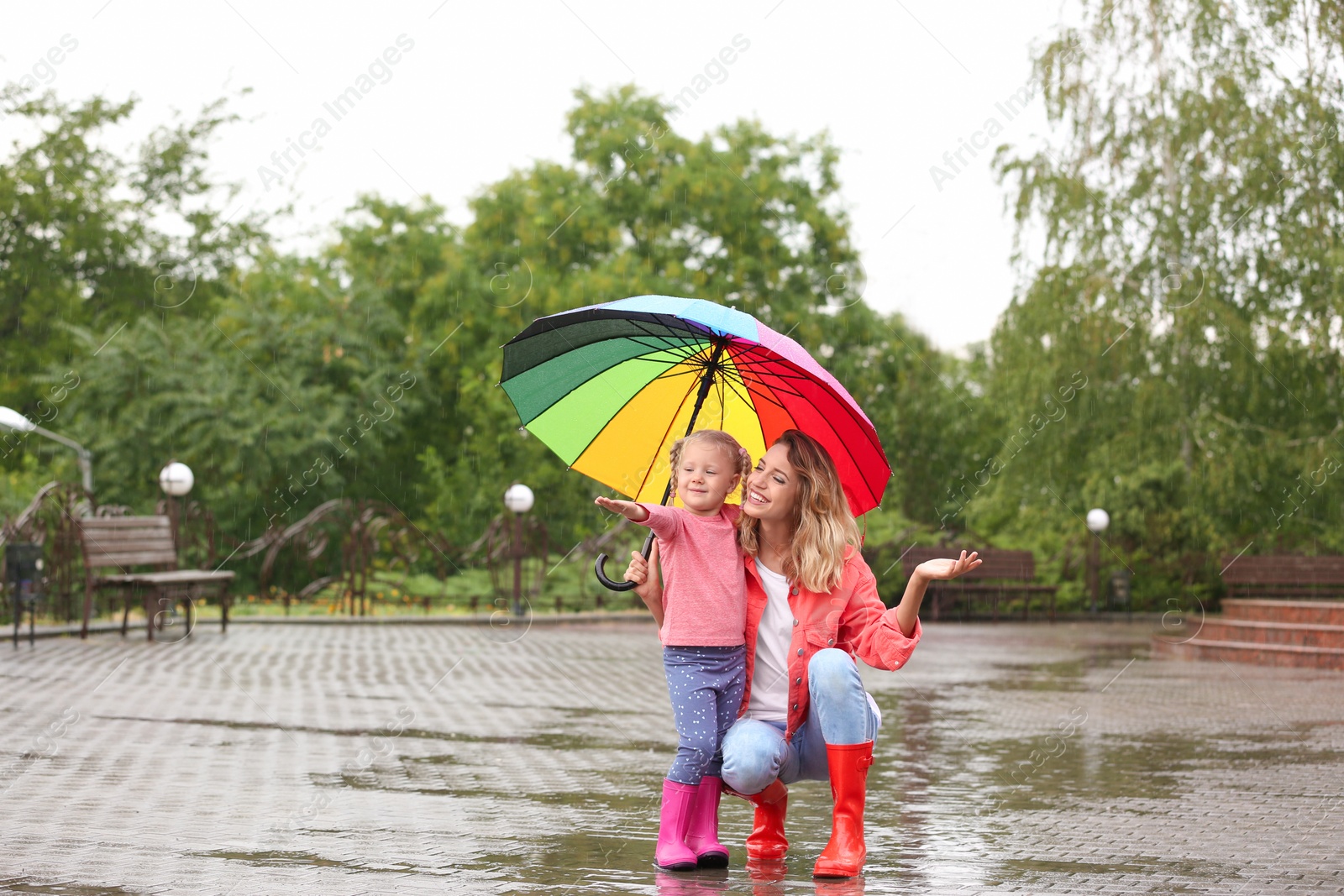 Photo of Happy mother and daughter with bright umbrella under rain outdoors