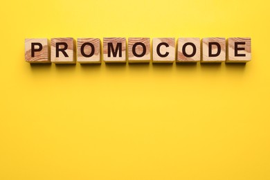 Word Promocode made of wooden cubes with letters on yellow background, top view. Space for text