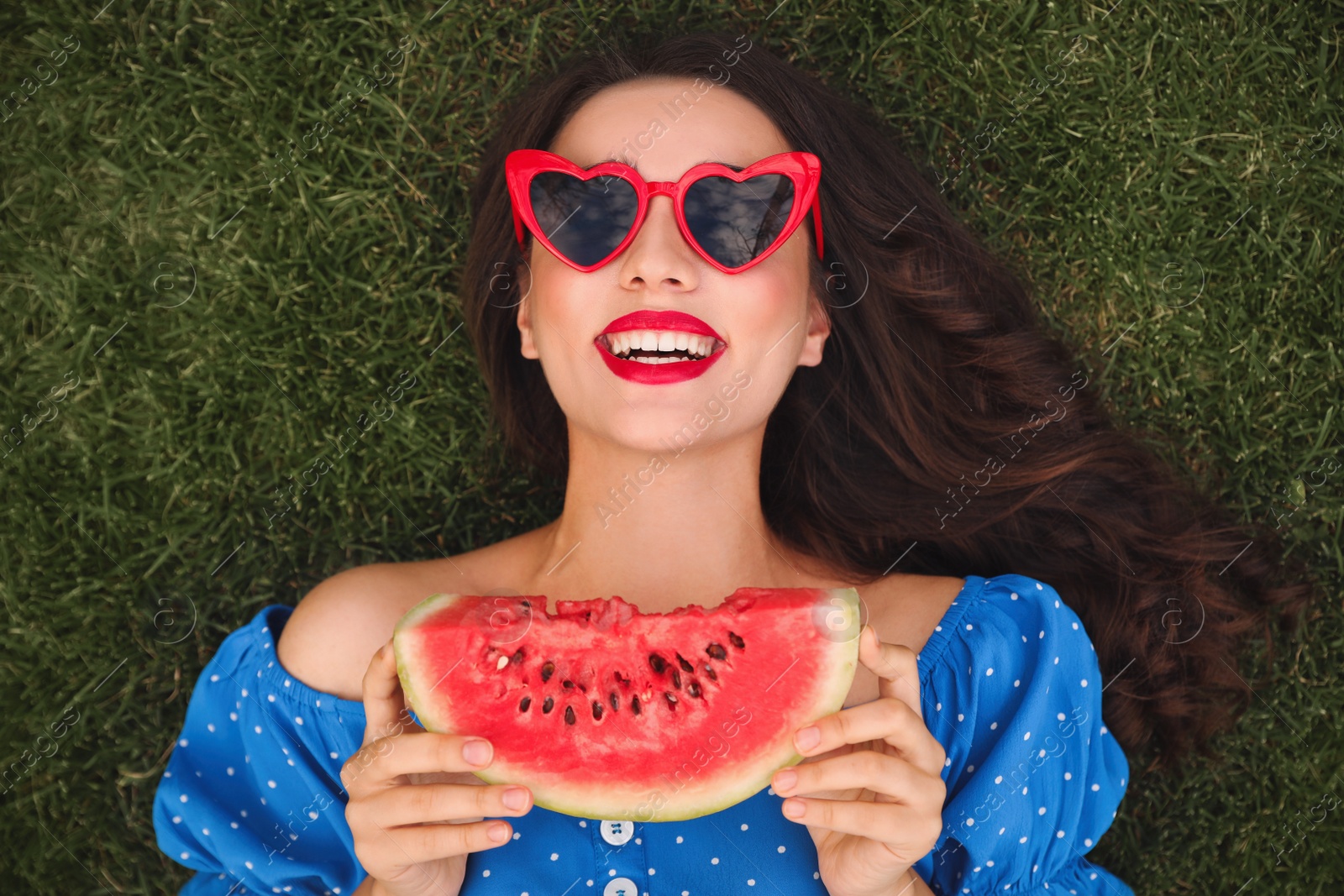 Photo of Beautiful young woman with watermelon on green grass outdoors, top view