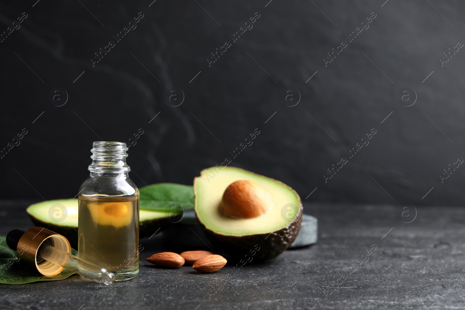 Photo of Essential oil, avocado and almonds on black table. Space for text