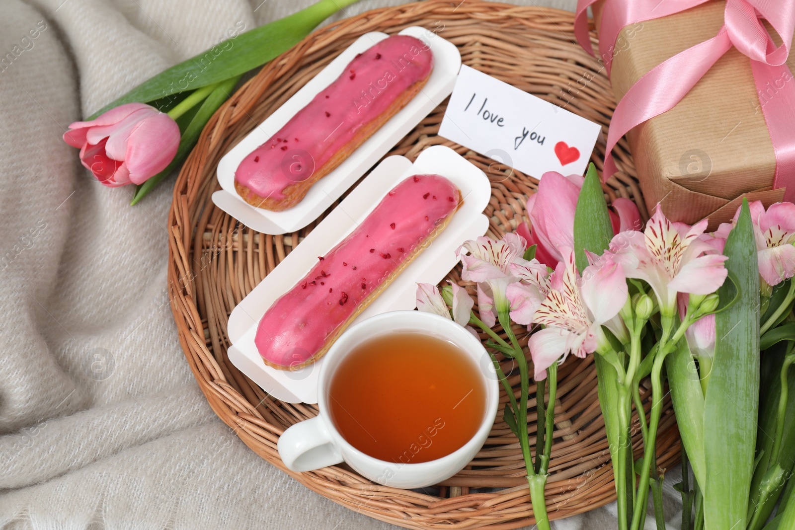 Photo of Tasty breakfast served in bed. Delicious eclairs, tea, flowers, gift box and card with phrase I Love You on blanket