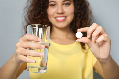 Photo of African-American woman with glass of water and vitamin pill against light grey background, focus on hands