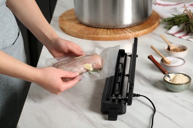 Photo of Woman using sealer for vacuum packing in kitchen, closeup. Sous vide cooking