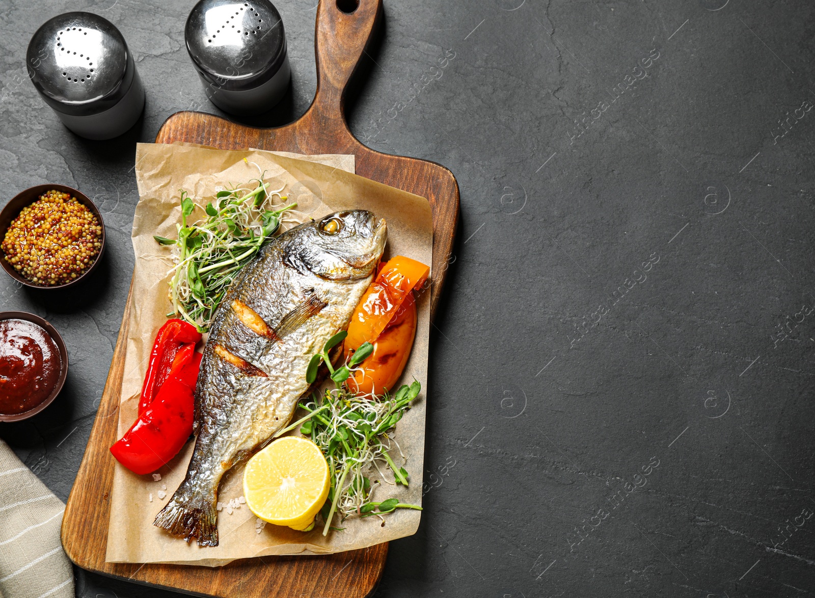 Photo of Delicious roasted fish and vegetables on dark grey table, flat lay. Space for text
