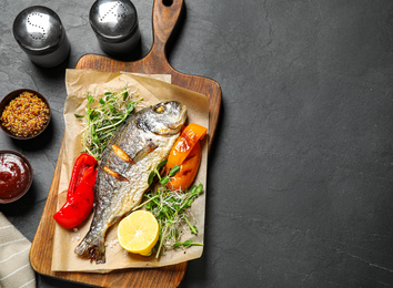 Photo of Delicious roasted fish and vegetables on dark grey table, flat lay. Space for text