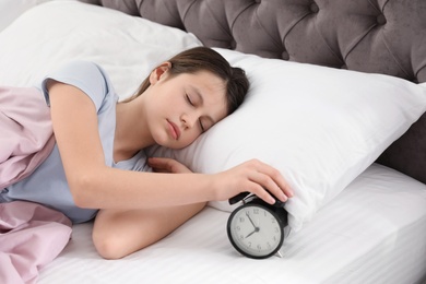 Photo of Beautiful little girl turning off alarm clock in bed