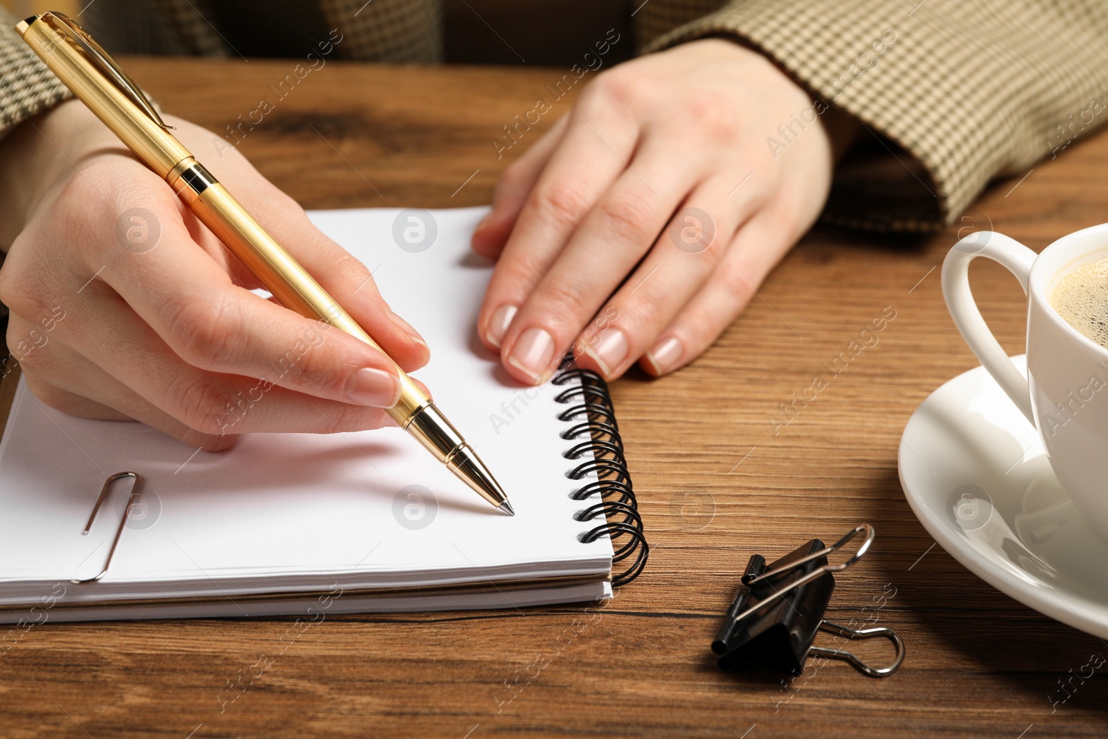 Photo of Woman writing in notebook at wooden table, closeup