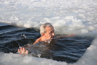 MYKOLAIV, UKRAINE - JANUARY 06, 2021: Mature man immersing in icy water on winter day