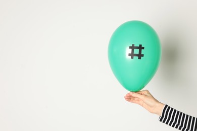 Photo of Woman holding green balloon with paper hashtag symbol on white background, closeup